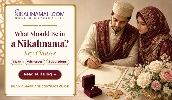 A Muslim groom in an ivory sherwani and maroon shawl signs a gold-bordered nikahnama beside his bride in a maroon and gold hijab, with a ring box, gold coins and roses on the table, illustrating NikahNamah's guide to what should be in a nikahnama, including mahr, witnesses and stipulations.